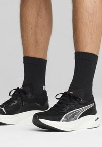 Black athletic shoes with mesh upper, white accents, lace-up design, and cushioned sole. Socks are black with ribbed texture and logo.