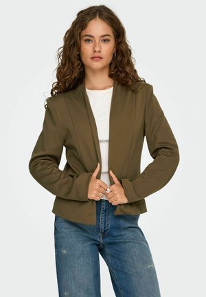Olijfgroene blazer met een minimalistisch ontwerp, gestructureerde schouders en lange mouwen. Gemaakt over een witte top met een gladde textuur.