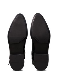 Semelles d'une paire de chaussures habillées noires à bouts pointus avec de petits talons, présentant la marque Calvin Klein sur la partie lisse de la semelle.