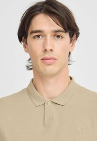Polo beige realizzato in tessuto testurizzato, con patta a tre bottoni e logo minimalista sul lato sinistro del petto.