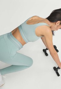 Light blue sports bra and matching leggings with a smooth texture, featuring white accent stripes, on a person using black dumbbells.