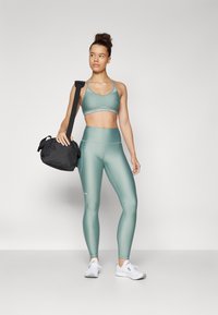 Sout bra e leggings verde menta in un tessuto liscio ed elastico. Borsa a spalla nera. Sneakers bianche con un design semplice.