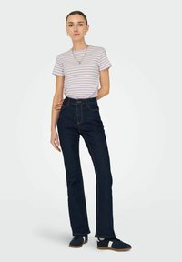Højtaljede mørkeblå jeans med let flare, parret med en lavendel- og hvidstribet t-shirt, og mørke sneakers med cremefarvede detaljer.