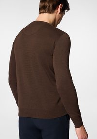 Brązowy sweter z prążkowaną fakturą, okrągłym dekoltem i dopasowanymi mankietami. Tył gładki, z minimalnymi szwami, w połączeniu z ciemnymi spodniami.