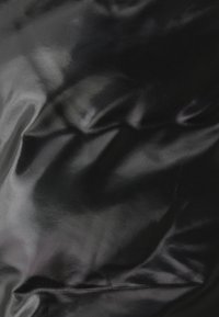 Svart glansigt syntetiskt tyg med en slät textur, som har subtila veck och en sydd söm längs ena kanten.