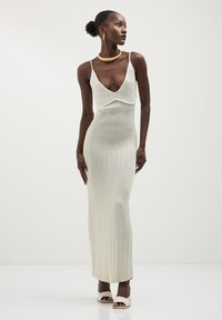 Abito maxi in maglia argento, con scollatura a V profonda e texture a coste. Accentuato da spalline sottili e silhouette aderente.
