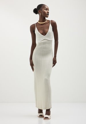 Knit maxi dress in silver, featuring a deep V-neck and ribbed texture. Accented with spaghetti straps and a fitted silhouette.
