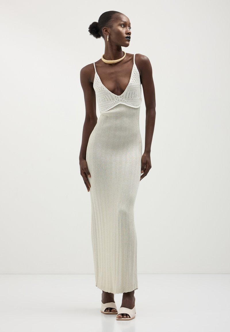 Abito maxi in maglia argento, con scollatura a V profonda e texture a coste. Accentuato da spalline sottili e silhouette aderente.