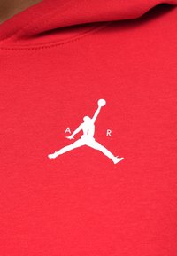 Červená mikina s hladkou texturou, která obsahuje bílé logo Jumpman a text "AIR" nad ním. Jednoduchý, výrazný design bez dalších vzorů.