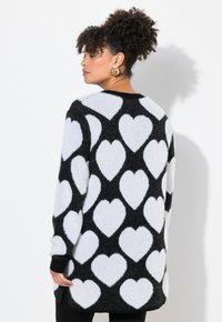 Zwart-witte sweater met een textuur breid ontwerp en grote witte hartpatronen. Lange mouwen, losse pasvorm en geribbelde halslijn.