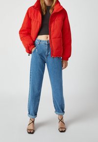 Rød pufferjakke med høj krave, parret med lys blå højtaljede jeans. Outfittet har sorte strop sandaler og en cropped top.