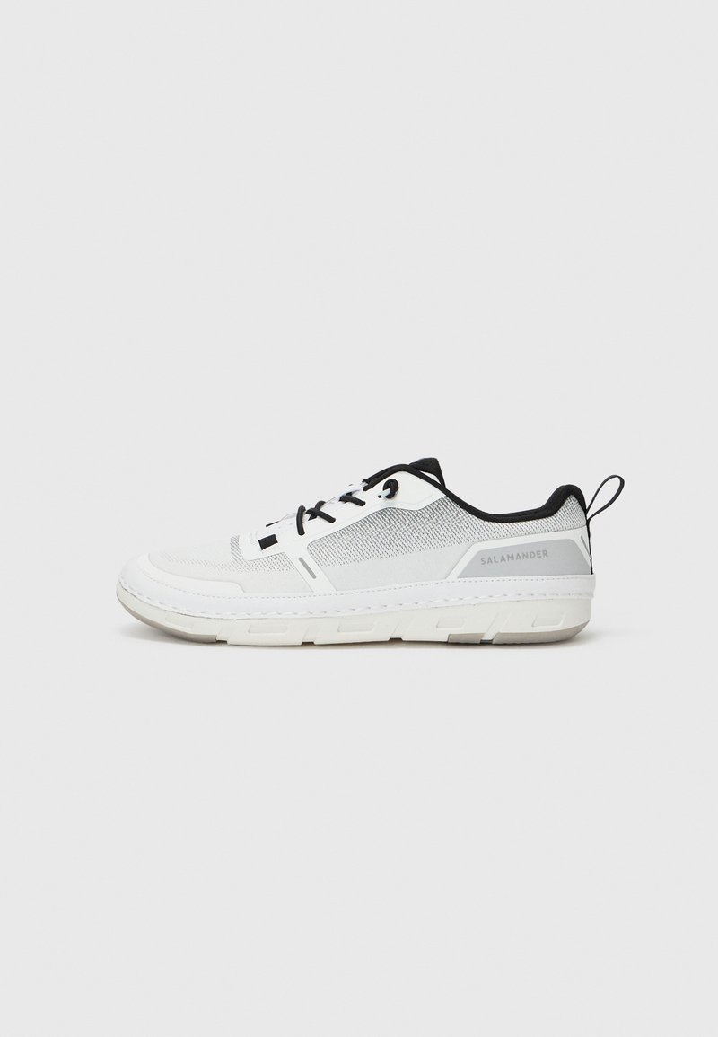 Weißer Sportschuh mit schwarzen Akzenten, Obermaterial aus Mesh, runde Zehenpartie, strukturierte Sohle, Schnürsenkel und eine Schlaufe an der Ferse. Markenname sichtbar an der Seite.