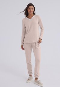 Jasno beżowy zestaw odzieży domowej składający się z długiego rękawa topu z dekoltem w serek oraz tapered spodni z elastycznym pasem i sznurkiem, wykonany z miękkiego, fakturowanego materiału.
