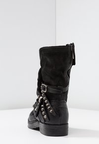 Svart ankelstövel med strukturerat tyg, silvernitar och spänndetaljer. Har dragkedja och låg klack.