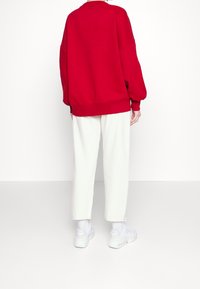 Sudadera roja de gran tamaño con hombros caídos y puños de canalé, combinada con pantalones blancos ajustados y zapatillas blancas.