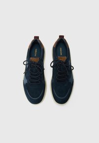 Navy blue sneakers with suede and fabric upper, brown accents, round toe, flat rubber sole, and laces for adjustable fit.