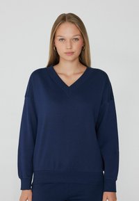 Sudadera en azul marino con cuello en V, fabricada en tejido suave, con mangas largas, puños acanalados y un ajuste holgado con dobladillo elástico.