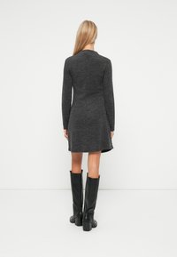 Rochie tricotată gri cărbune, cu mâneci lungi și margine evazată. Poartă ciocate negre din piele până la genunchi, cu toc pătrat și gros.