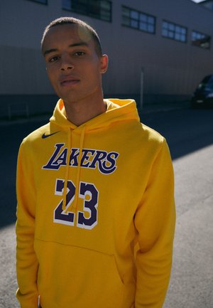 Gelbe Kapuzenjacke mit "LAKERS" und "23" in lila Druck. Der Stoff ist weich, hat eine Fronttasche und eine Kapuze mit Zugbändern. Einfaches Design.
