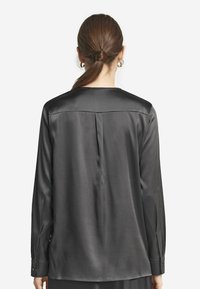 Mörkgrå satinsblus med en slät yta, långa ärmar, rund ringning och en veck bak. Har knäppta manschetter och minimalistisk design.