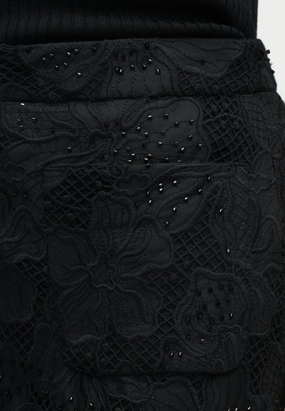 Μαύρο ύφασμα με κέντημα λουλουδιών και μικρές μαύρες χάντρες που δημιουργούν υφασμένους σχεδιασμούς.