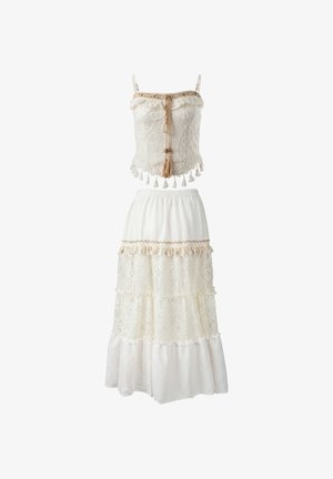 Zweiteiliges weißes Spitzenoutfit mit ärmellosem Crop-Top mit Quasten und mehrlagigem langem Rock mit Spitze und dekorativem Besatz.