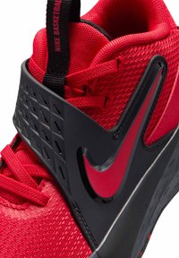 Czerwony but do koszykówki z chropowatą siateczkową cholewką, czarną gumową śródpodeszwą z geometrycznymi wzorami oraz wyraźnym czerwonym logo Nike.