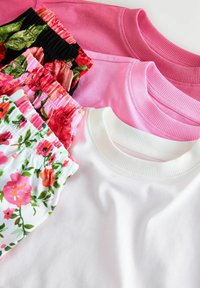 Four short-sleeve tops in pink and white, featuring ribbed crew necks, alongside patterned floral shorts with elastic waistbands.
