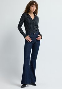 Černobílá pruhovaná košile s knoflíky a límečkem, doplněná tmavě modrými džínami s vysokým pasem a rozšířenými nohavicemi. Na nohou jsou černé boty na vysokém podpatku.