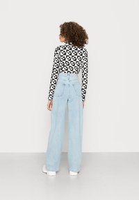 Top de manga longa preto e branco com padrão e gola alta, combinado com jeans de perna larga azul claro de cintura alta e sapatos brancos robustos.