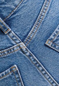 Denimová tkanina světle modré barvy s křížovým vzorem a kontrastním oranžovým šitím, doplněná o dva přední kapsy.