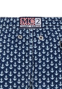 Pantaloni da bagno blu con un motivo ripetuto di ancore bianche, dotati di due occhielli argentati, un'etichetta con il marchio e cuciture a contrasto.