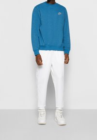 Felpa blu con maniche lunghe e scollatura rotonda, abbinata a pantaloni sportivi bianchi con righe laterali e scarpe da ginnastica bianche.