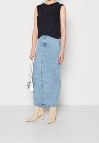 Svart ärmlös stickad topp med texturerade mönster, ihop med en högmidjad ljusblå denimkjol och beige ankelboots. Vit handväska ingår.