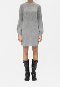 Abito grigio lavorato a maglia con maniche lunghe, scollatura rotonda e vestibilità rilassata. Abbinato a stivali alti neri in gomma lucida con fibbie.