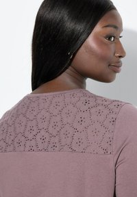 Fialové tričko s texturovaným krajkovým zadním dílem s květinovými výřezy, krátkými rukávy a měkkou, hladkou tkaninou.