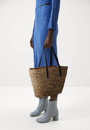 Geflochtener Strohtasche mit schwarzen Griffen, kombiniert mit einem blauen, gerippten Kleid und hellblauen, hochhackigen Stiefeletten. Sauberes und zeitgemäßes Design.