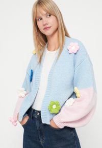 Ανοιχτό μπλε πλεκτό κάρντιγκ με υπερμεγέθη ροζ και μπλε λουλουδάτα απλικέ, ριμπ μανσέτες και σχέδιο με μπλοκ χρωμάτων που περιλαμβάνει ροζ μανίκια.