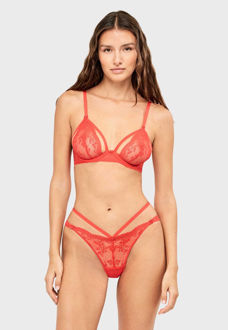Rode kanten bralette met verstelbare bandjes en driehoekige cups; bijpassende rode kanten string met gedurfde banddetails. Zachte textuur en bloemmotief.