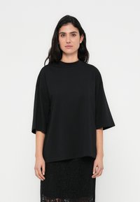 T-shirt preta oversize feita de tecido macio com gola redonda e mangas até ao cotovelo, combinada com uma saia preta de renda texturizada.