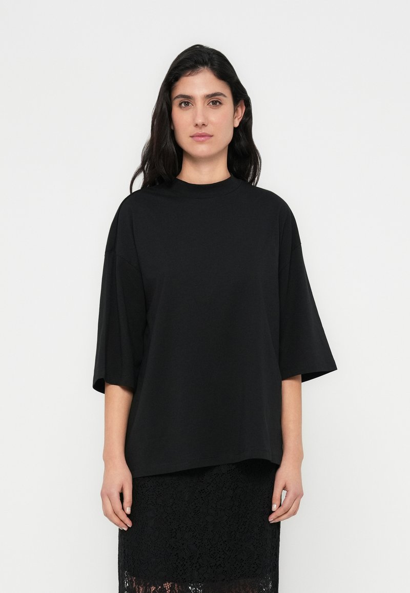 T-shirt preta oversize feita de tecido macio com gola redonda e mangas até ao cotovelo, combinada com uma saia preta de renda texturizada.