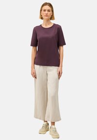 Korte mouw, ronde hals paarse t-shirt van zachte stof, gecombineerd met losse beige linnen broeken en lichtgekleurde sneakers.