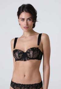 Reggiseno in pizzo nero con motivi floreali, supporto con ferretto e spalline in satin con dettagli in metallo. Elementi di design trasparenti e texturizzati.