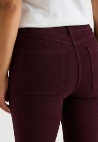 Vaqueros burdeos con un acabado de denim texturizado. Incluye bolsillos traseros estándar y una silueta ajustada. Cintura con trabillas para cinturón.