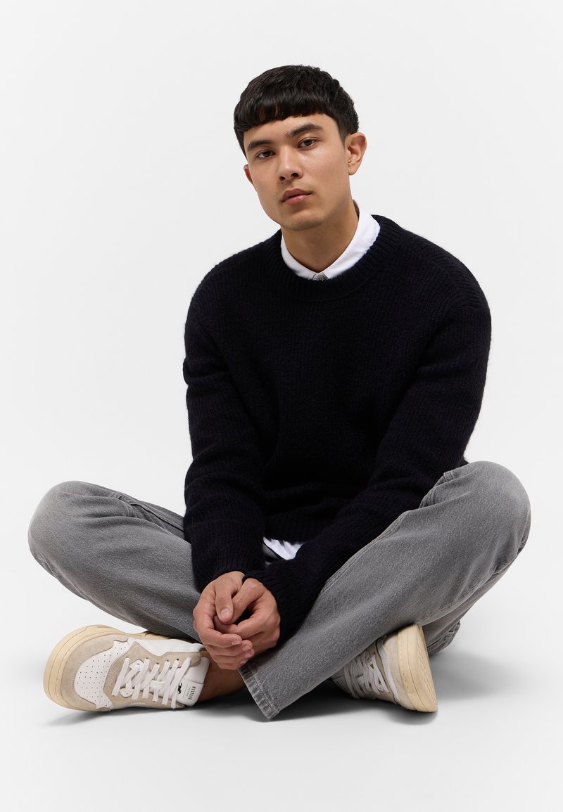 Granatowy sweter z dzianiny, szare dżinsowe spodnie i kremowe sneakersy. Sweter ma okrągły dekolt; sneakersy mają teksturalne akcenty i sznurowadła.