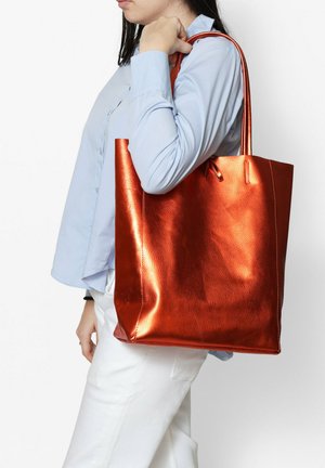 Sac fourre-tout orange métal fabriqué en matériau texturé, avec deux longues anses et un design simple sans embellissements.