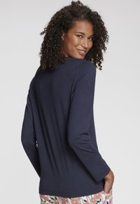 Navy blue long-sleeve top with a relaxed fit, round neck, and smooth texture. Paired with patterned floral pants at the waist.
