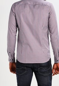 Kostkovaná košile s dlouhým rukávem v červené, bílé a modré barvě s manžetou na knoflíky, doplněná tmavě modrými džínami s designem zadní kapsy.