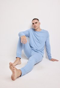 Lichtblauwe loungewear set bestaande uit een langetermijn top met borstzak en bijpassende strakke broek, gemaakt van zachte, gladde stof.