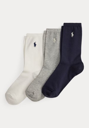 Trois chaussettes montantes pliées en blanc, gris et bleu marine, chacune avec un petit logo brodé d'un joueur de polo près de la cheville.